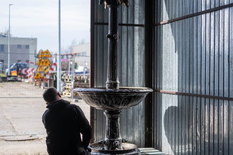 Metalowa fontanna stoi w hangarze, czyści ją męzczyzna.