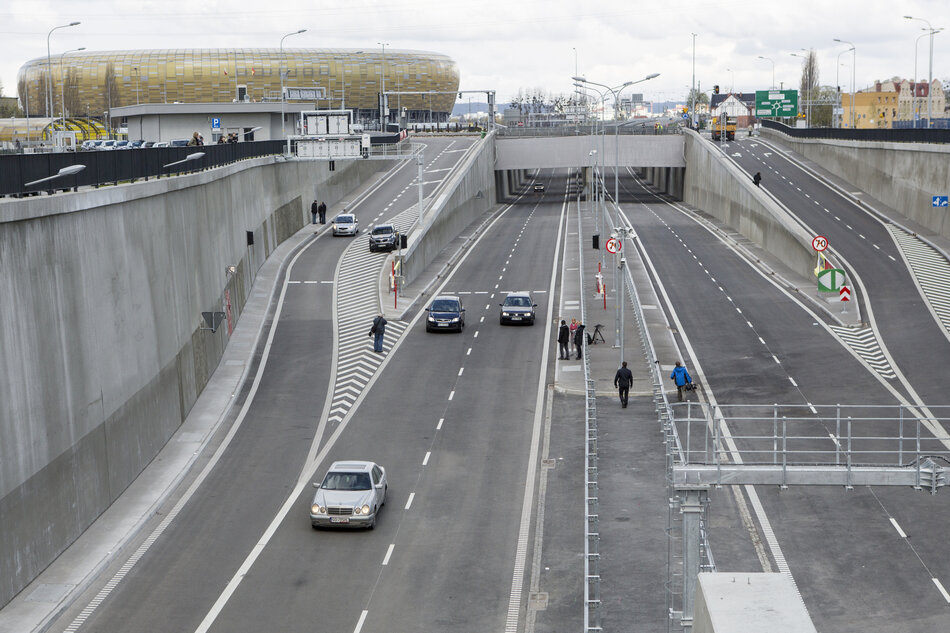 Wyjazd z tunelu drogowego. Po jezdni jadą samochody. W tle stadion.