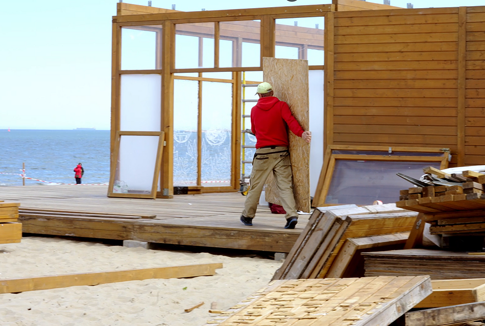 Mężczyzna przenosi sklejkę drewna na budowie beach baru na plaży w Brzeźnie
