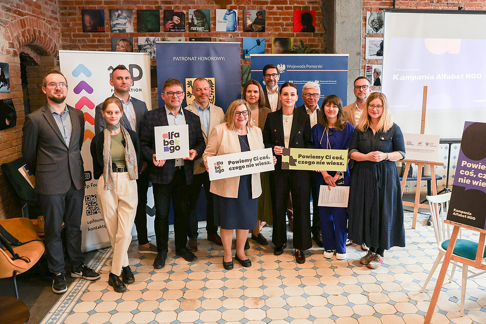 Kilkanaście osób pozuje do zdjęcia w kawiarni.