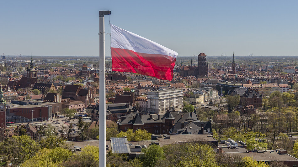 biało czerwona flaga powiewa nad miastem, które widać w tle
