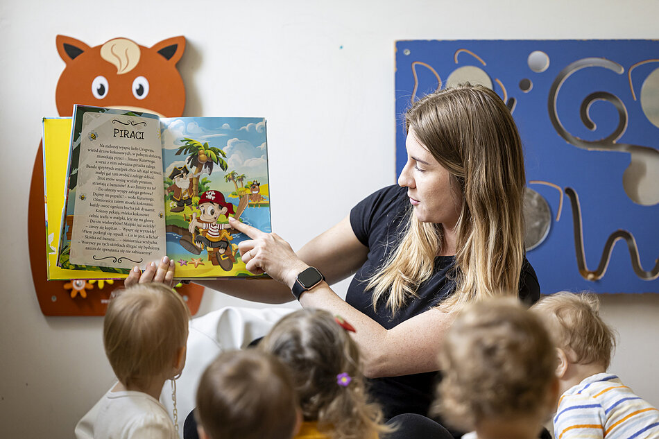 na zdjęciu nauczycielka pokazuje małym dzieciom ilustrację w książce
