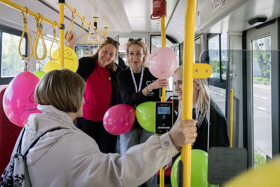 Udekorowane balonami wnętrze tramwaju, w środku rozmawiają ludzie.