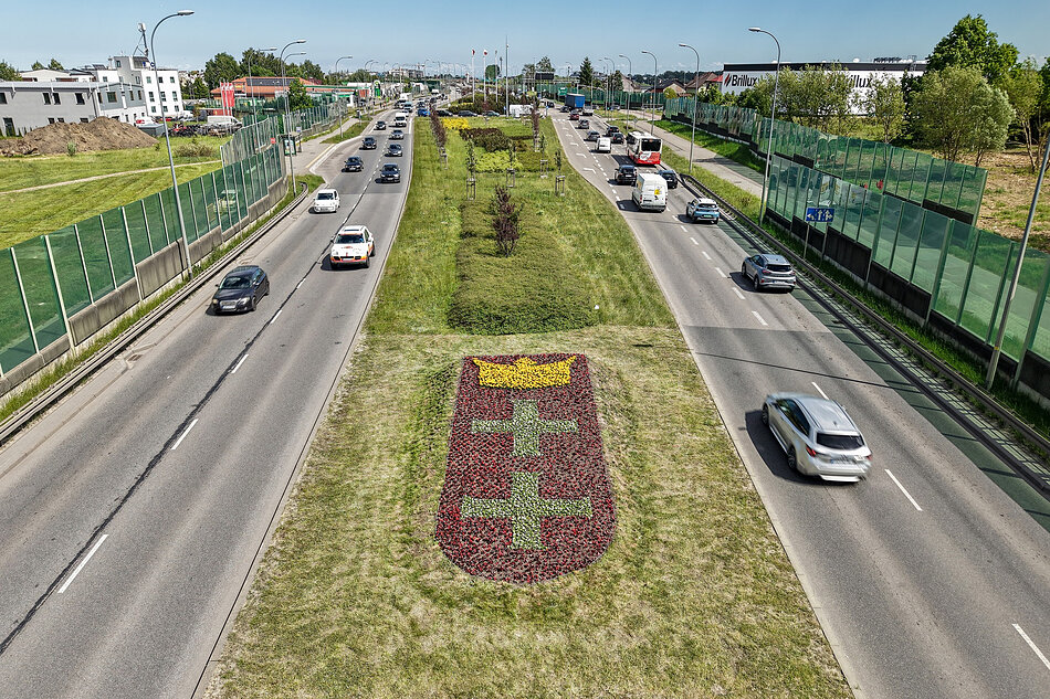 Zdjęcie z lotu ptaka, widok na pas zieleni w ciągu dwóch ulic, pomiędzy którymi widać kompozycję kwiatową, tworząca herb Gdańska.