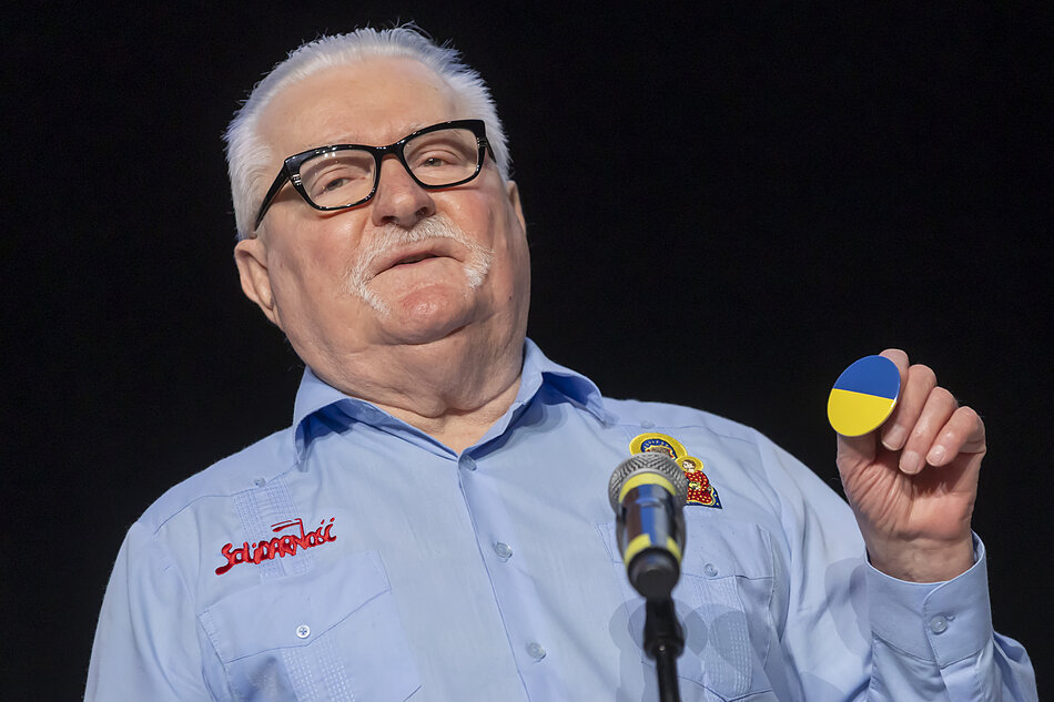 Na zdjęciu Lech Wałęsa z okrągłym niebiesko-żółtym znaczkiem w dłoni 