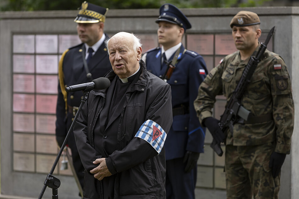 ksiądz przy mikrofonie, za nim strażnik miejski, żołnierz i policjant przy pomniku
