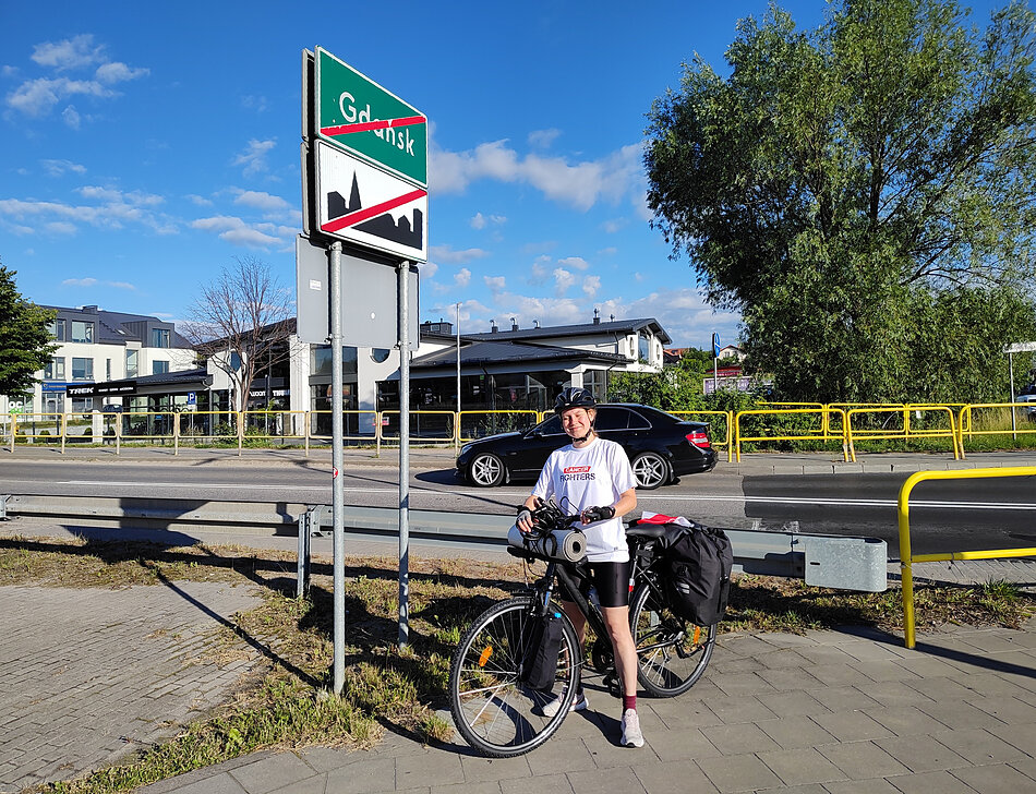 Dziewczyna na rowerze obok tabliczki informującej o wyjeździe z miasta Gdańsk. 