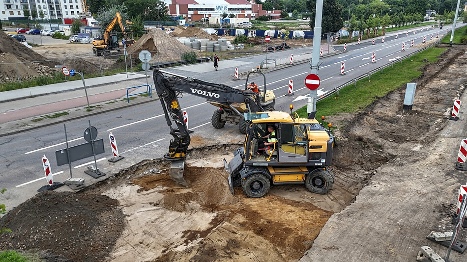 zdjęcie z drona, widać rozkopany jeden pas jezdni, obok normalna asfaltowa jezdnia, na środku stoi żółta koparka
