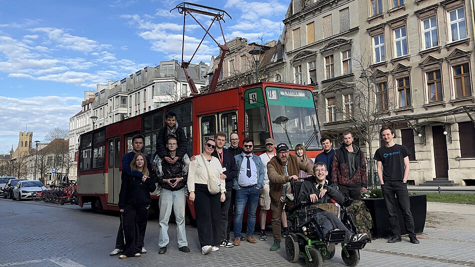 Kilkanaście osób pozuje do zdjęcia przed starym tramwajem w starej dzielnicy miasta.