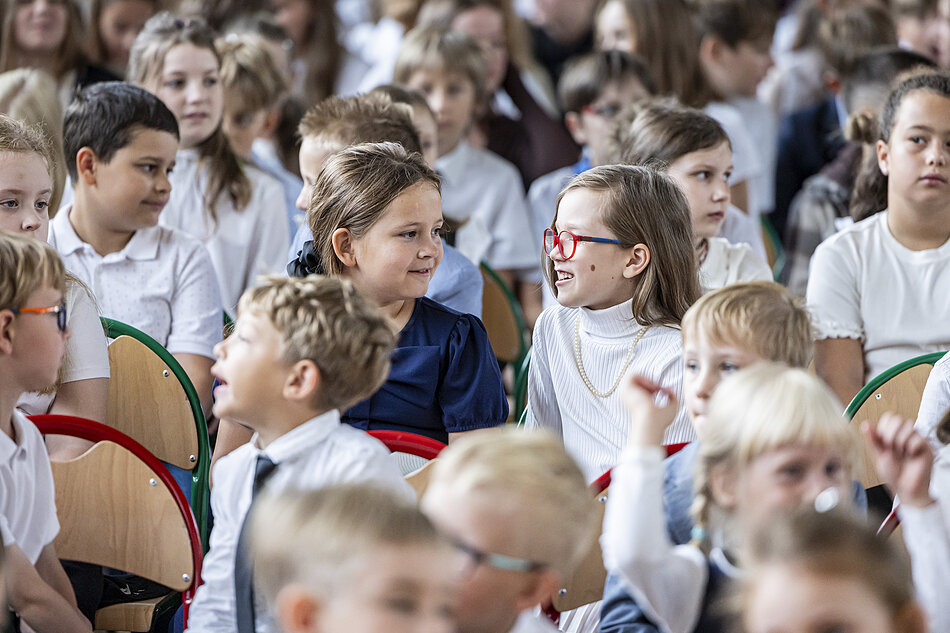 Miejska Inauguracja Roku Szkolnego 2026/2027. Dzieci siedzą na sali i rozmawiają ze sobą.