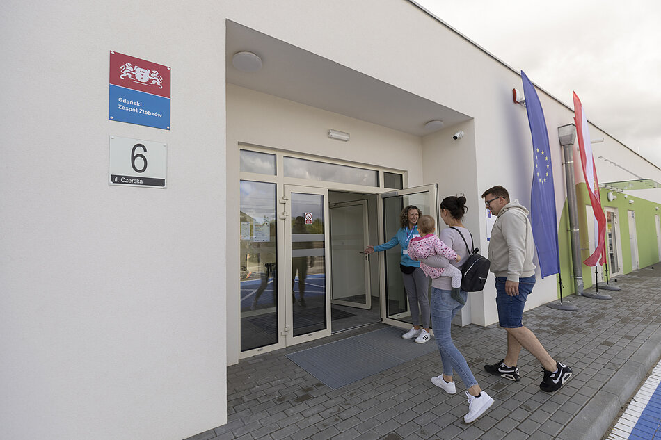 Kobieta w drzwiach żłobka wita rodziców z dzieckiem.