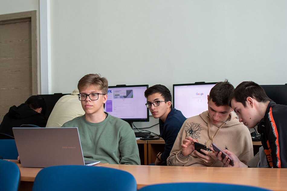 Pięciu nastolatków korzystających z laptopów i smartfonów w nowoczesnej klasie