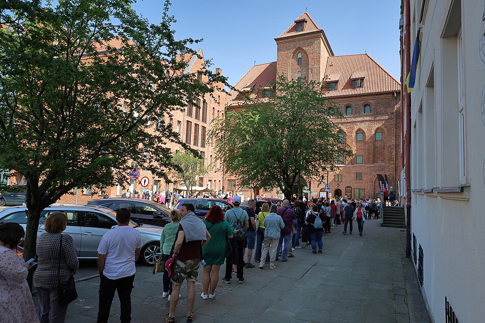 Kolejka ludzi do zabytkowego budynku w mieście.