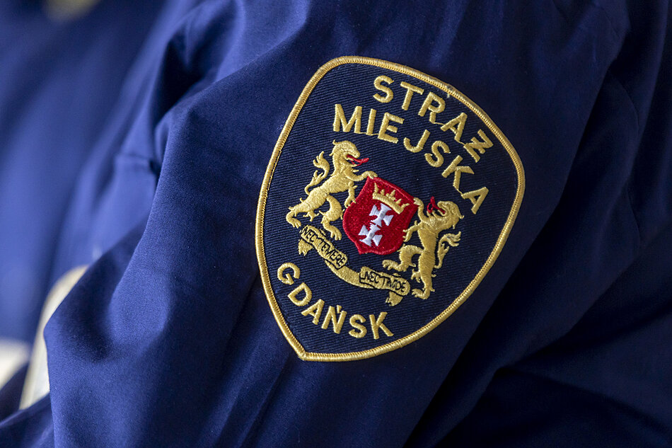 na zdjęciu fragment granatowego munduru strażnika miejskiego z widoczną odznaką naszytą na ramieniu