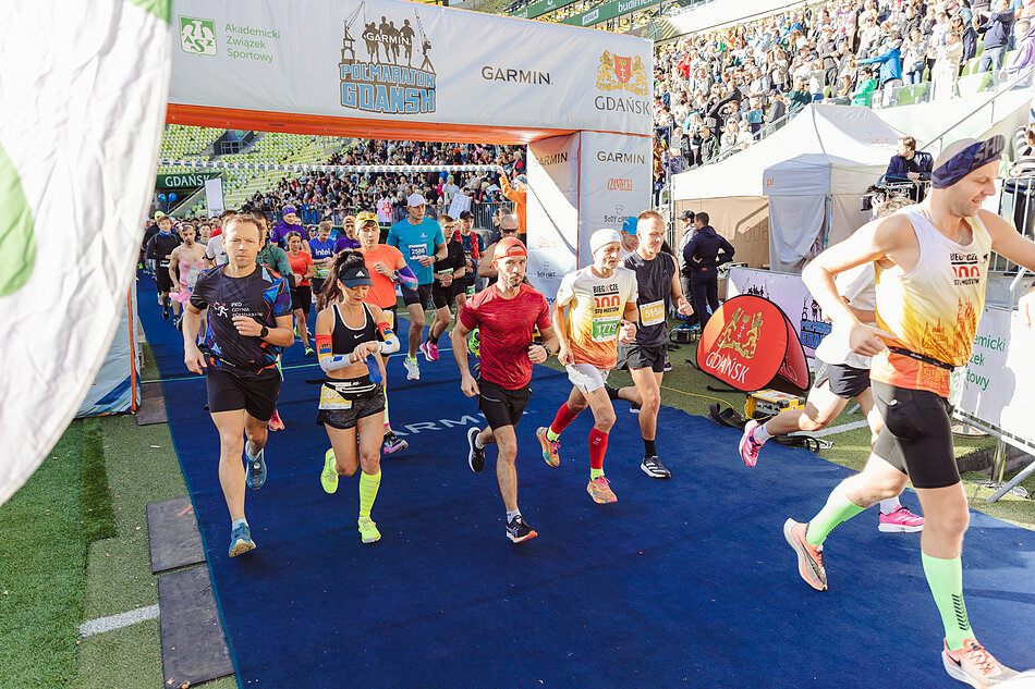 Garmin Półmaraton Gdańsk. Na zdjęciu ludzie biorą udział w biegu. Za nimi widać linię startową. 