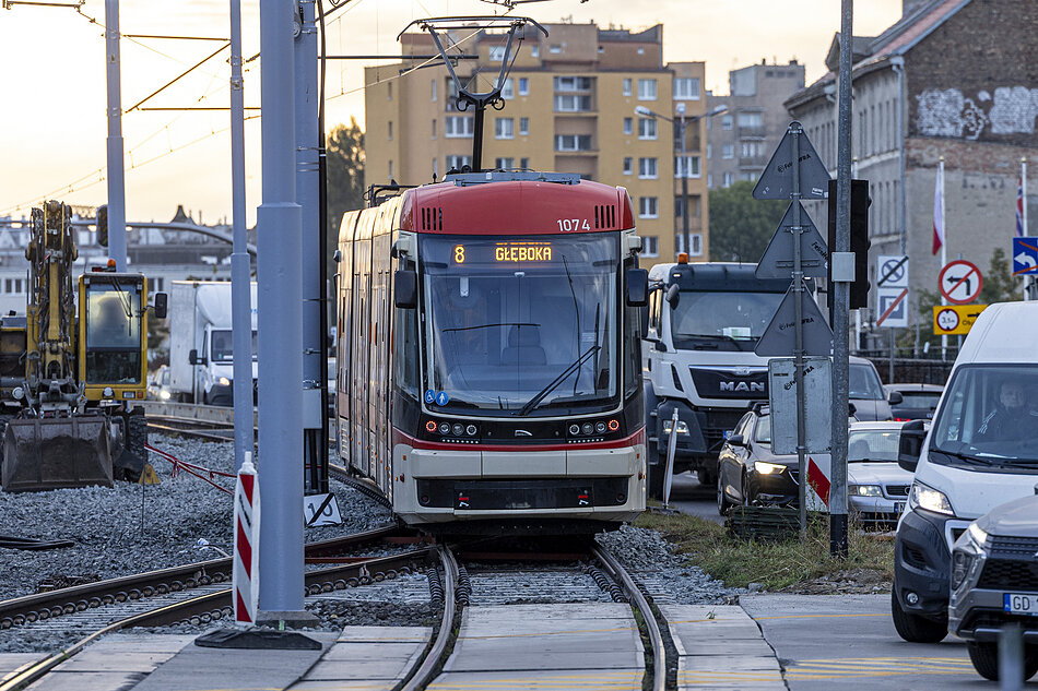 czerwono-biały tramwaj na torze tramwajowym w mieście. tramwaj ma numer 8 z przodu i napisane na nim słowo głęboka wydaje się być nowoczesnym tramwajem elektrycznym o eleganckim wzornictwie. po prawej stronie jest ruchliwa ulica z samochodami i ciężarówkami.