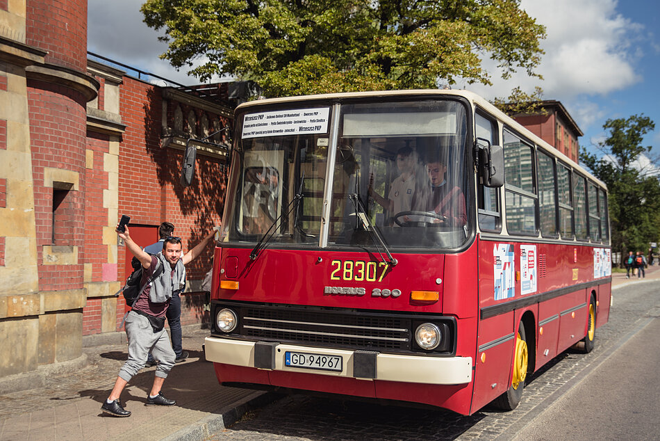 Autobus Ikarus na przystanku, przed nim podskakuje uradowany człowiek.