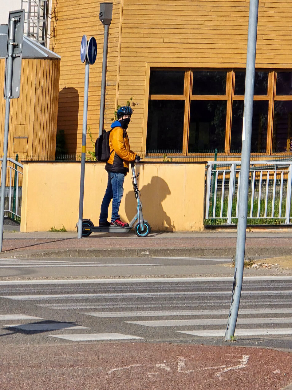 Mężczyzna w kominiarce i kasku jadący na hulajnodze elektrycznej