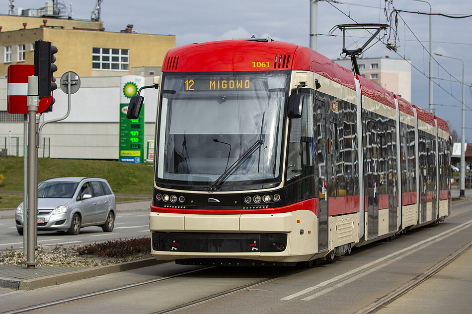 na zdjęciu biało czerwony tramwaj stojący przed sygnalizacją świetlną, w tle po lewej samochód osobowy