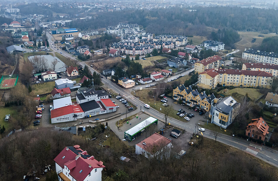 lotnicze zdjęcie ulicy otoczonej zielenią, i domami, w oddali widoczne osiedla mieszkaniowe
