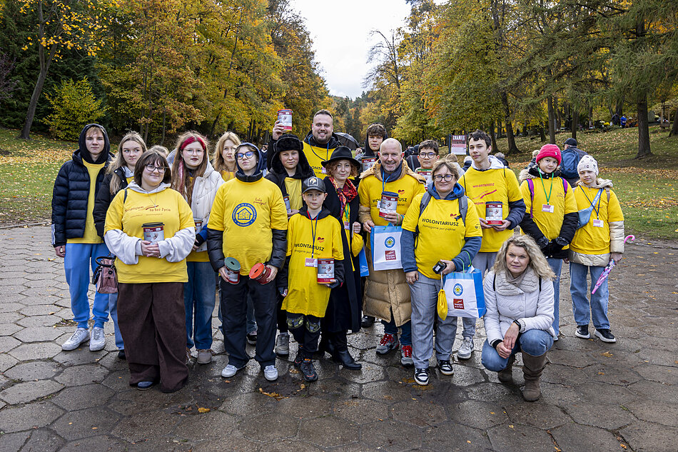 Grupa kilkunastu osób w żółtych koszulkach wolontariuszy pozuje do zdjęcia na cmentarzu.