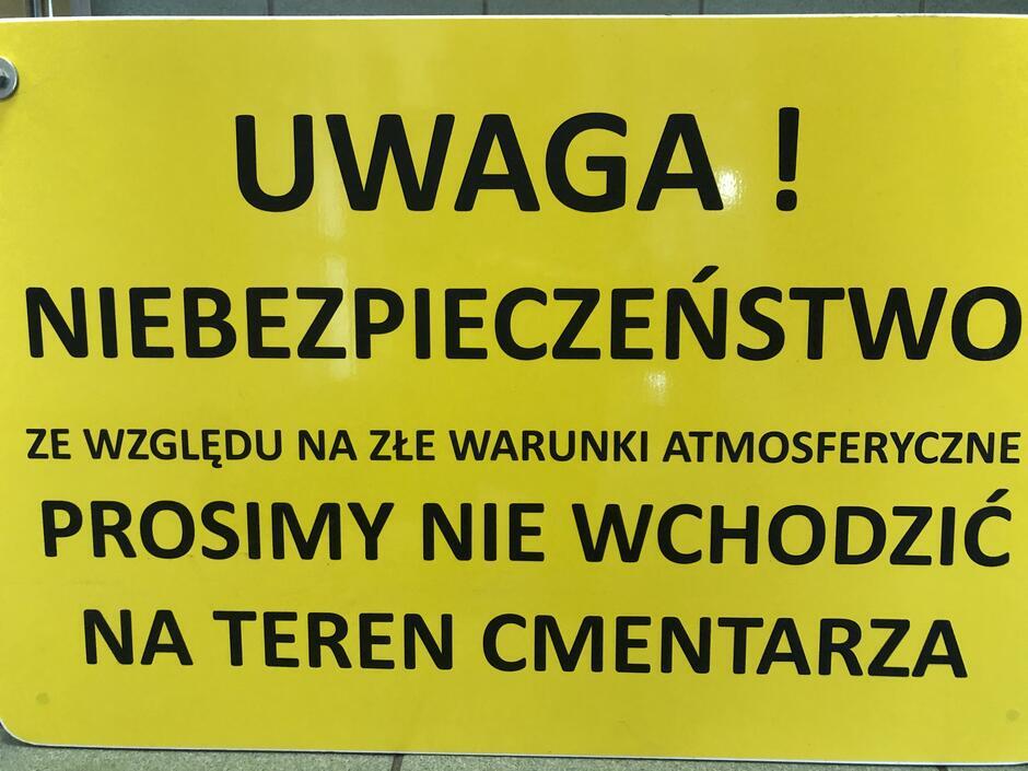 Na zdjęciu widoczna jest tabliczka z napisem: Uwaga, niebezpieczeństwo! Ze względu na złe warunki atmosferyczne prosimy nie wchodzić na teren cmentarza 
