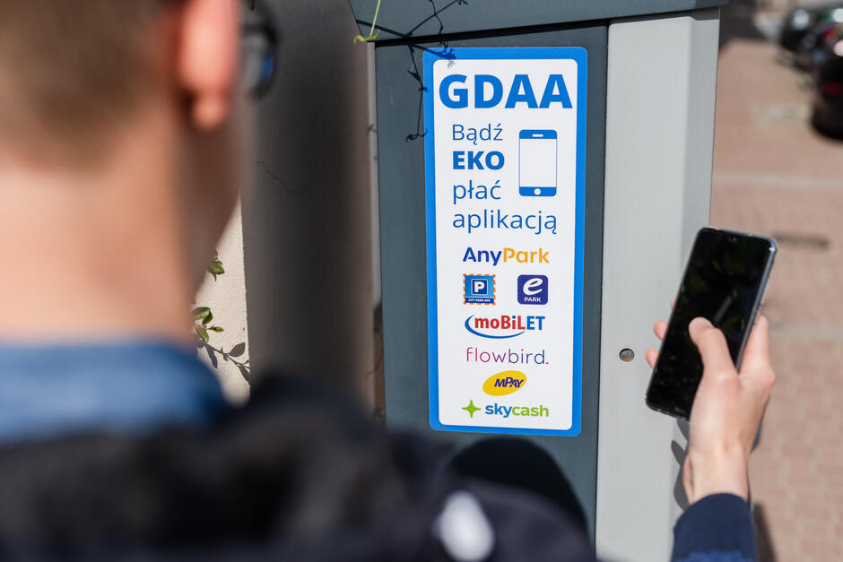 Na zdjęciu widoczna jest naklejka na parkometrze z nazwami obsługiwanych w Gdańsku aplikacji mobilnych do wnoszenia opłat za postój