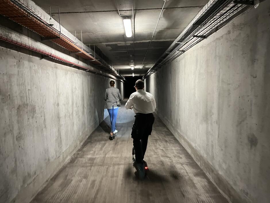 Na zdjęciu widoczne są dwie osoby - Pan Maciej i Pani Katarzyna, którzy przemierzają korytarz Tunelu na elektrycznych hulajnogach.
