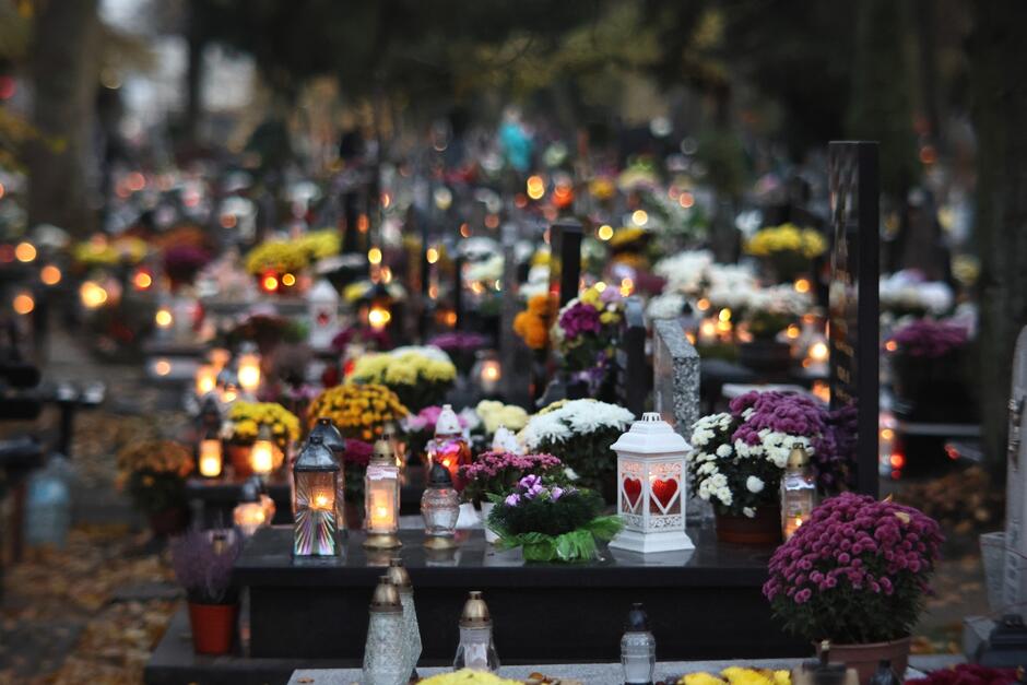 Na zdjęciu widoczne są groby z kwiatami i zniczami w Dniu Wszystkich Świętych 