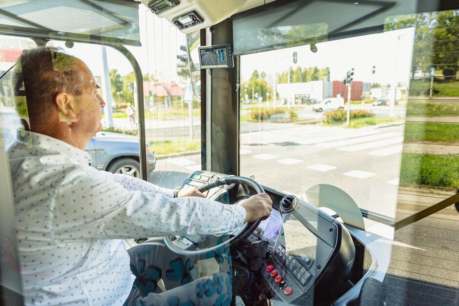 Na zdjęciu widoczny jest kierowca prowadzący autobus w kabinie