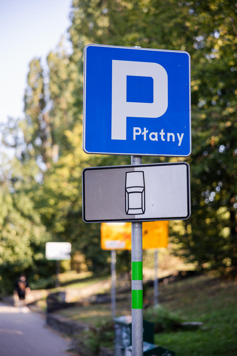 Na zdjęciu znajduje się znak parking z zieloną obwódką na słupku