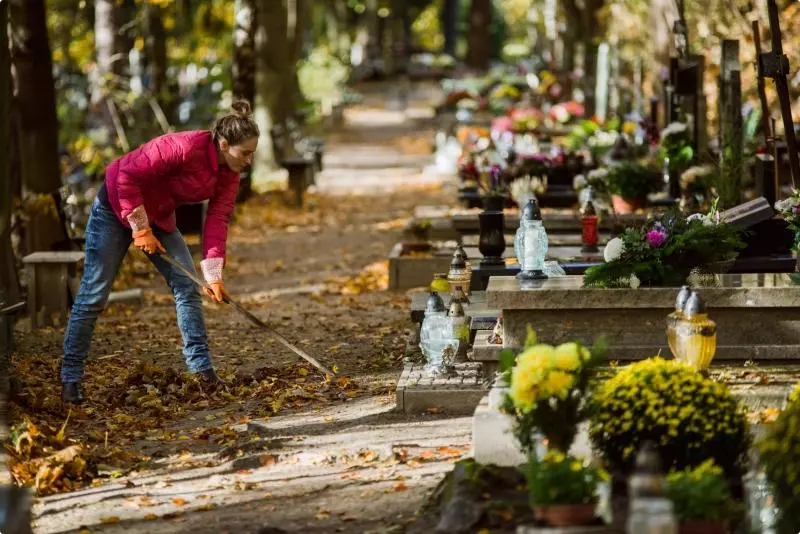 Idzie zima, instalacja wodociągowa zostaje wyłączona. Na zdjęciu widać kobietę porządkującą otoczenie nagrobka na cmentarzu.