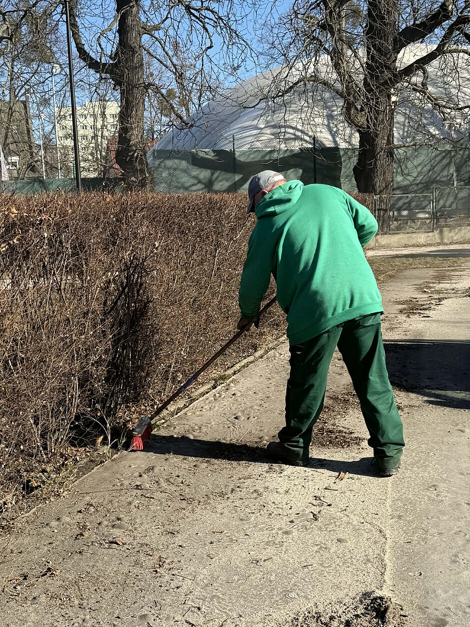 Na zdjęciu widoczny jest pracownik grabiący alejkę na zieleńcu