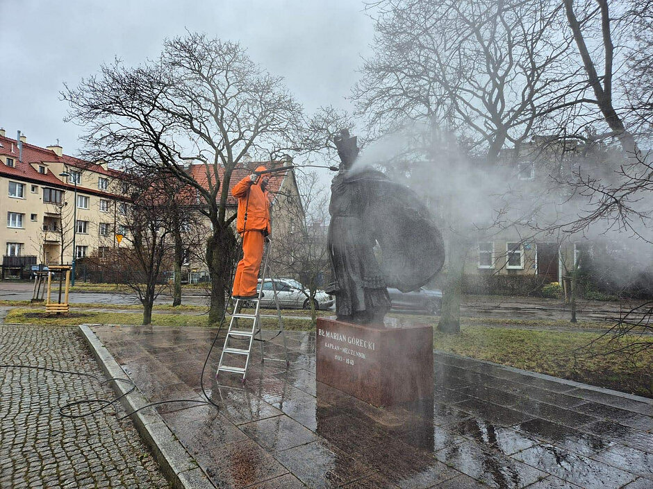 Na zdjęciu widać mężczyznę, który myjką ciśnieniową oczyszcza pomnik bł. ks. Góreckiego, gdańskiego męczennika. 