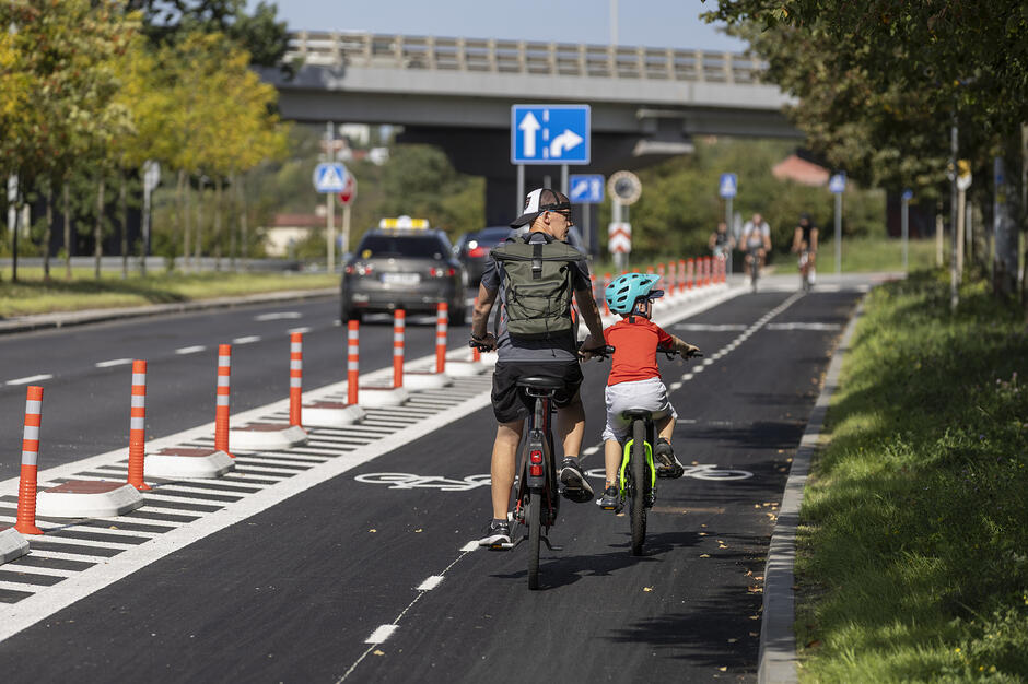 Droga rowerowa w Al. Sikorskiego, zieleń miejska oraz rodzic z dzieckiem na rowerze