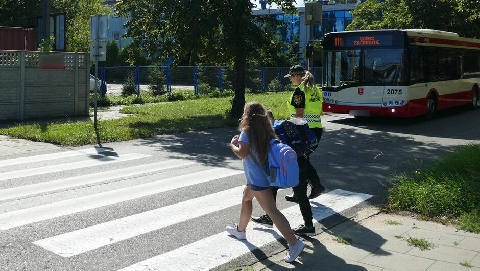 Strażniczka miejska przeprowadza dzieci przez przejście dla pieszych.JPG