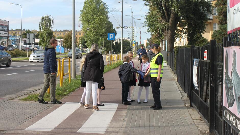 Strażniczka przy przejściu dla pieszych rozdaje dzieciom odblaski