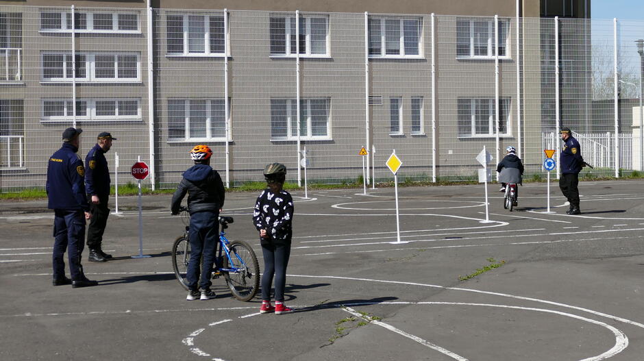 trzech straznikow na miasteczku obserwuje jak dwojka uczniow jezdzi na rowerach