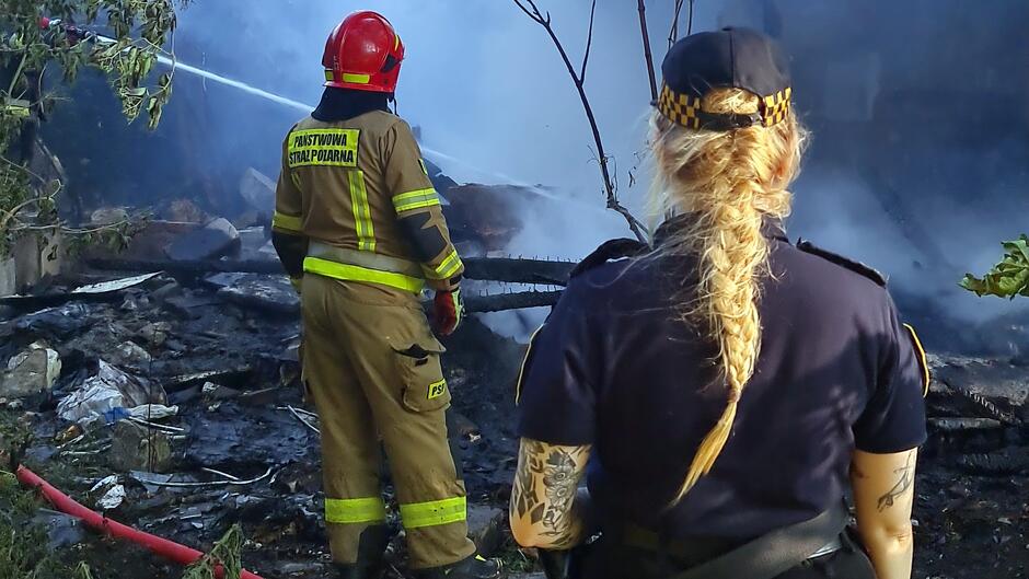 strażniczka stoi plecami do obiektywu, dalej strażak i pogożelisko