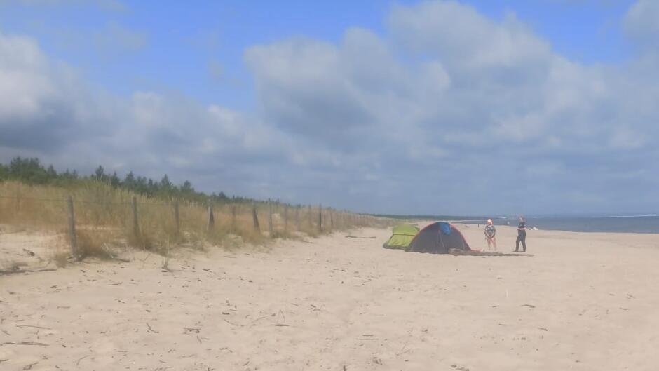 namioty na plaży obok nich stoi strażniczka i kobieta