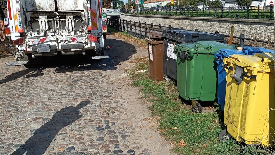śmieciarka i kontenery na odpady na brukowanej drodze