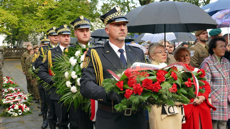 Strażnicy z wiązankami kwiatów.