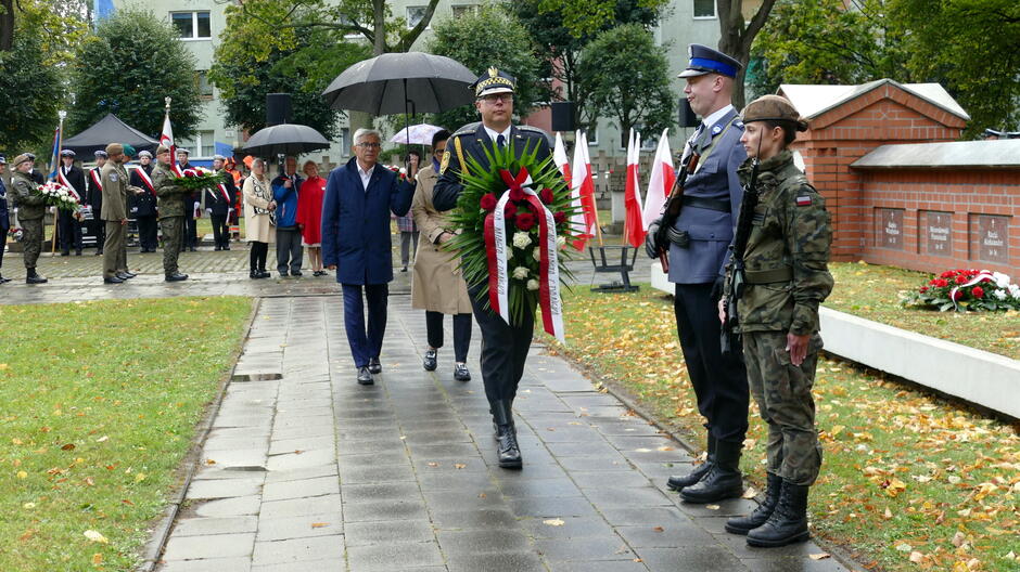 Warta honorowa przy grobach poległych pocztowców, strażnik miejski z wiązanką kwiatów. 