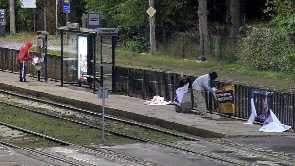 Dwie osoby zrywają plakaty wyborcze z przystanku tramwajowego. 