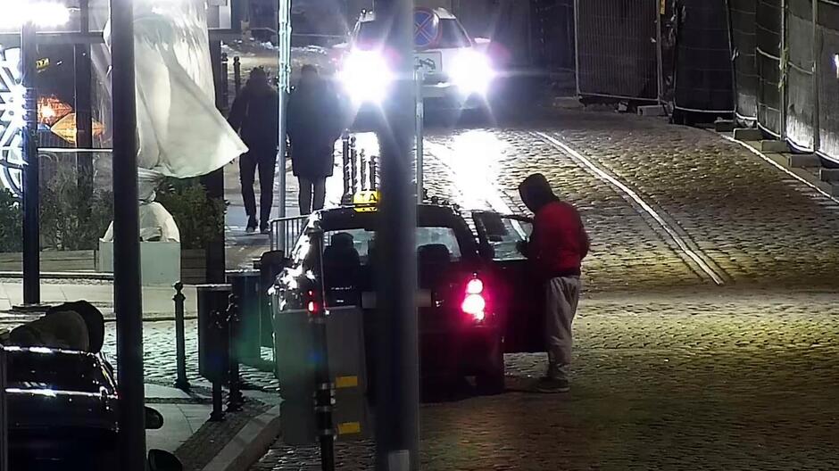 Mężczyzna w czerwonej kurtce wsiada nocą do taksówki.