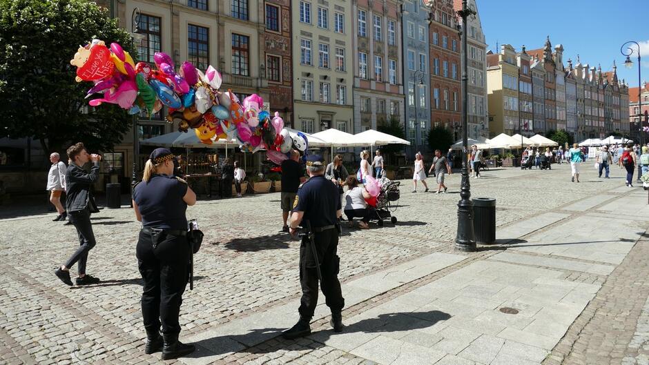 Strażnicy miejscy patrzą w kierunku osoby sprzedającej balony na Długim Targu w Gdańsku. 