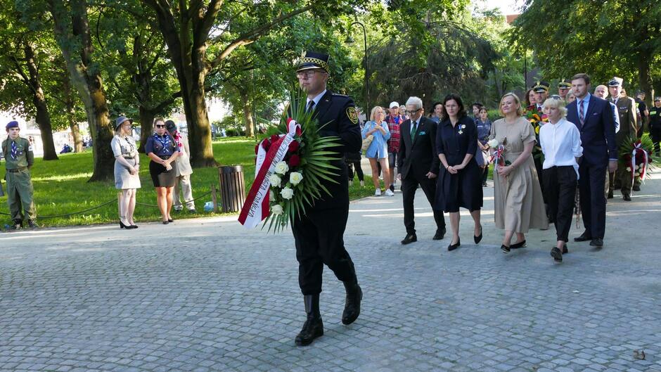 Strażnik miejski a za nim delegacja składają wieniec. 