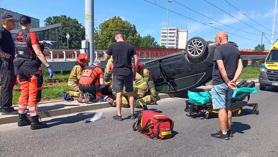 przewrócone auto, służby ratunkowe udzielają pomocy poszkodowanemu