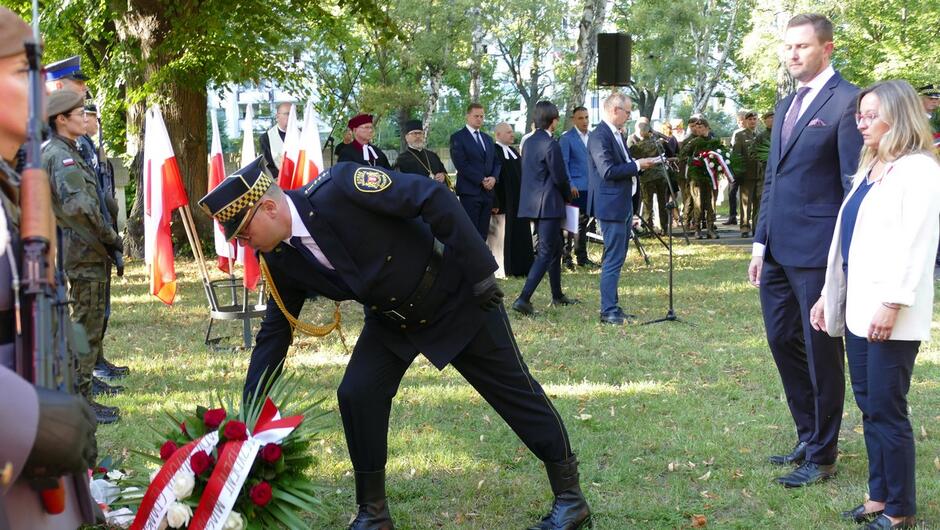 Strażnik miejski składa wieniec, za nim przedstawiciele władz miasta. 