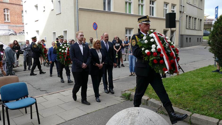 Strażnik miejski składa wieniec, za nim oficjalna delegacja. 